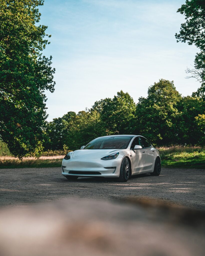 En stillastående vit tesla i grönskande svensk landskap